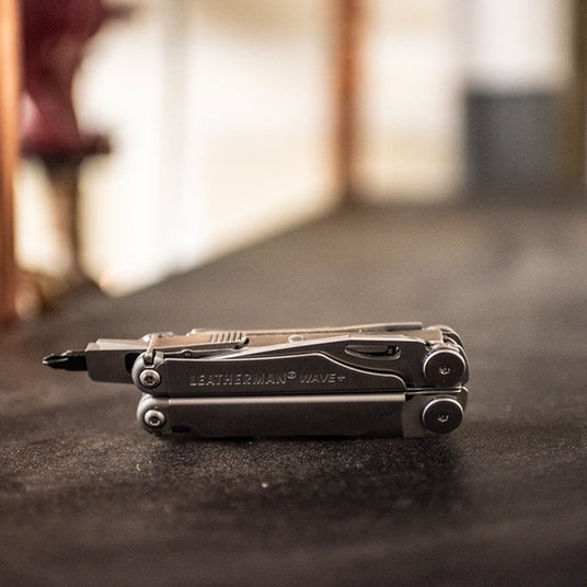 Translation missing: en.Closed Leatherman Wave+ multi-tool with screwdriver bit attachment resting on a workshop surface