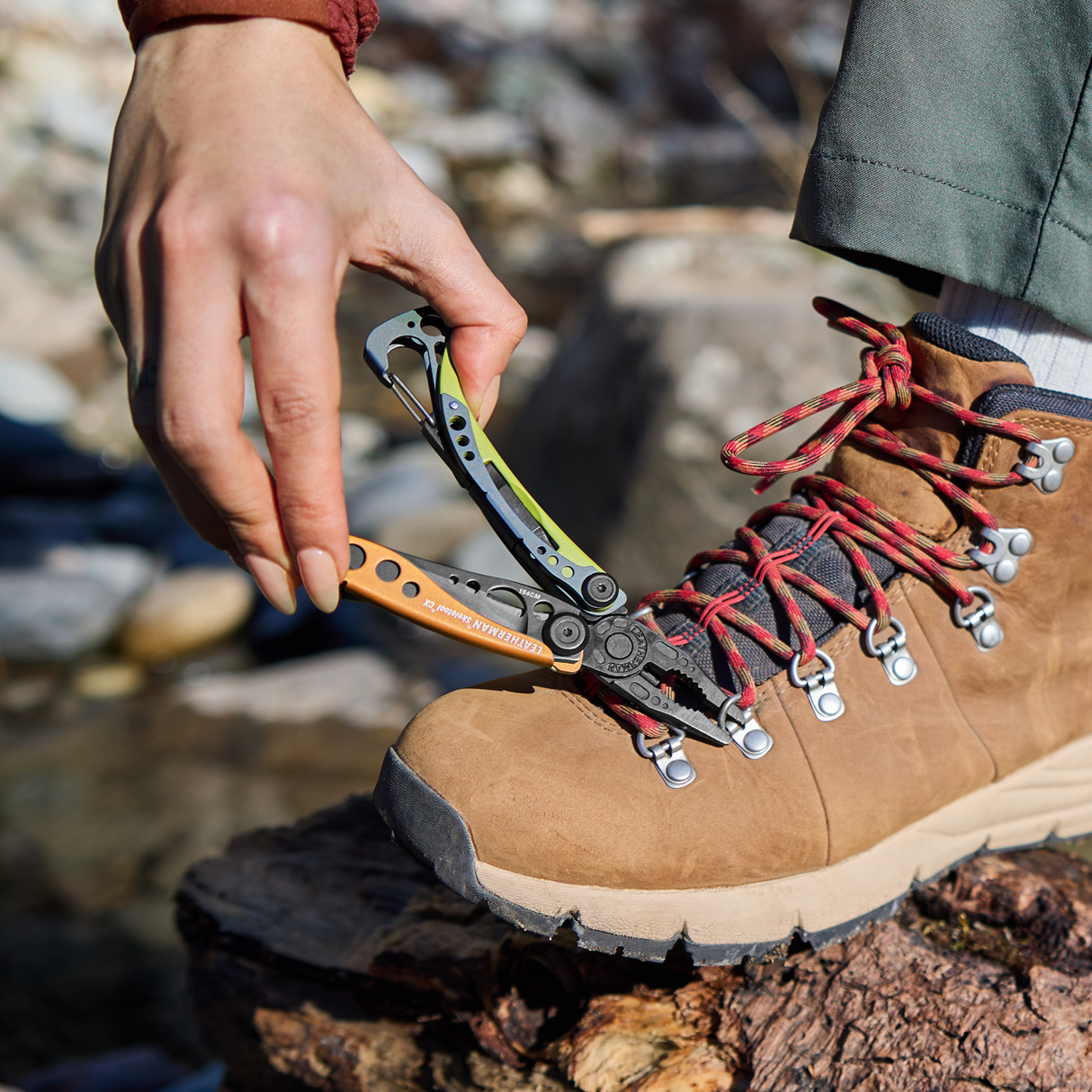 Translation missing: en.Person using a Leatherman Skeletool® CX in Aurora color to fix the lace hook on a hiking boot