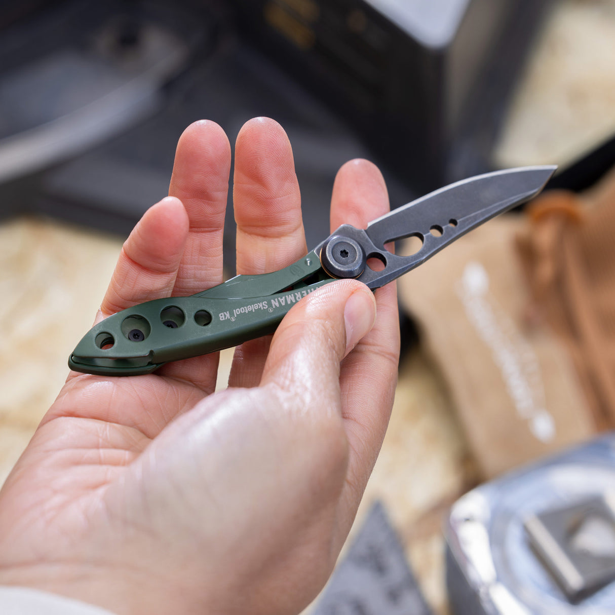 Translation missing: en.Hand holding an OD green Leatherman Skeletool KB folding knife with open blade