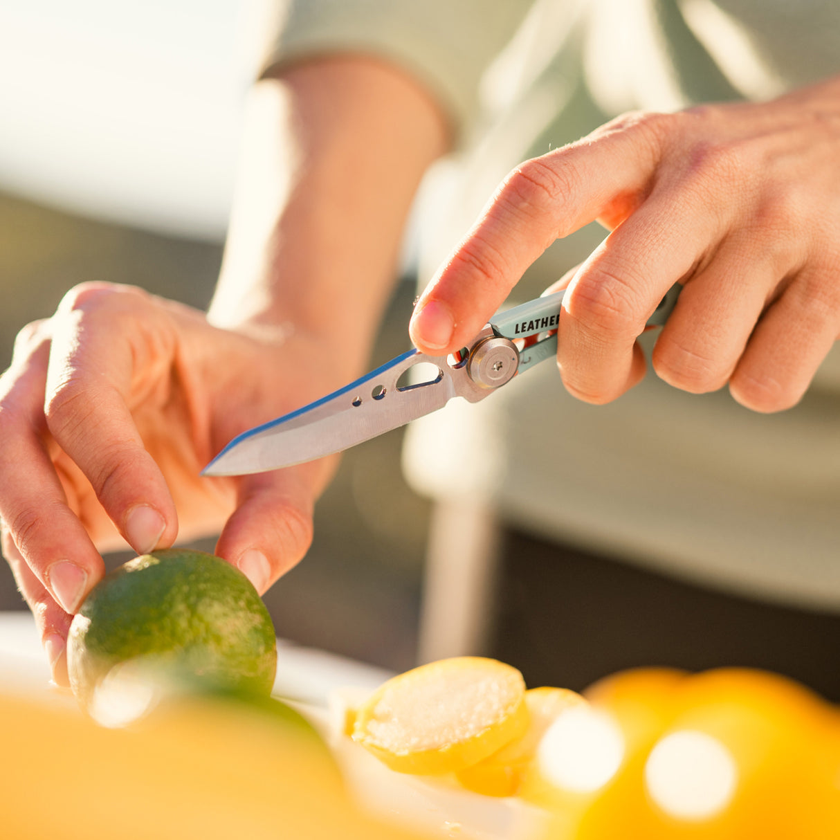 Translation missing: en.Person using an aqua Skeletool KB folding knife to slice a lime on a cutting surface outdoors