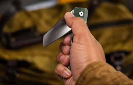 Translation missing: en.Hand holding an Okra Leatherman Glider™ folding knife against a backpack, showcasing its ergonomic design
