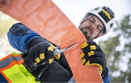 Translation missing: en.Service worker wearing safety gear and gloves using a Leatherman Raptor Rescue Shears to cut material outdoors, highlighting reliable tools for service men and women in demanding environments
