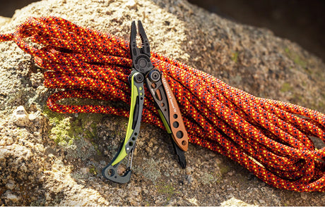 Translation missing: en.Leatherman Skeletool multi-tool resting on a rock beside a brightly colored climbing rope outdoors, representing versatile gifts under $100