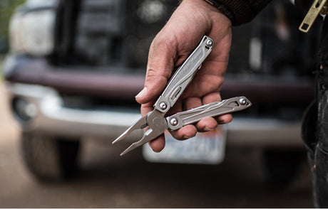 Translation missing: en.Person holding an open Leatherman Wingman multi-tool with pliers extended in front of a vehicle, showcasing practical gifts under $75