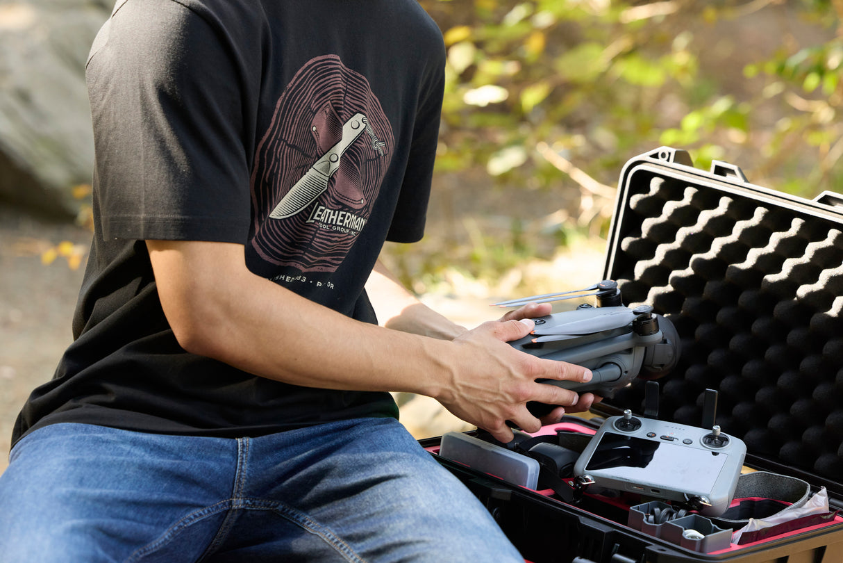 Translation missing: en.A person pulling a drone out of a carrying case while wearing a black Leatherman Blade &amp; Grain Tee with a fixed blade design on the front