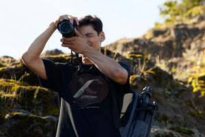 Translation missing: en.A photographer wearing a black Leatherman Blade &amp; Grain Tee while taking a pictures outdoors