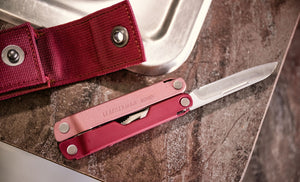 Translation missing: en.Heathered Cranberry Bond open showing knife blade and a Heathered sheath that is open next to a sink on the countertop