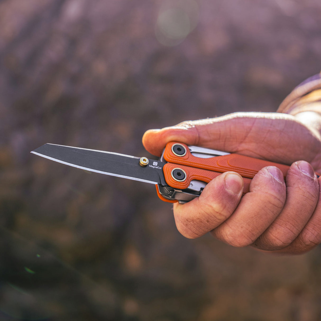 Translation missing: en.Canyonland Leatherman Wave® Alpha multi-tool held in hand, showcasing its sleek design and sharp blade against a natural background