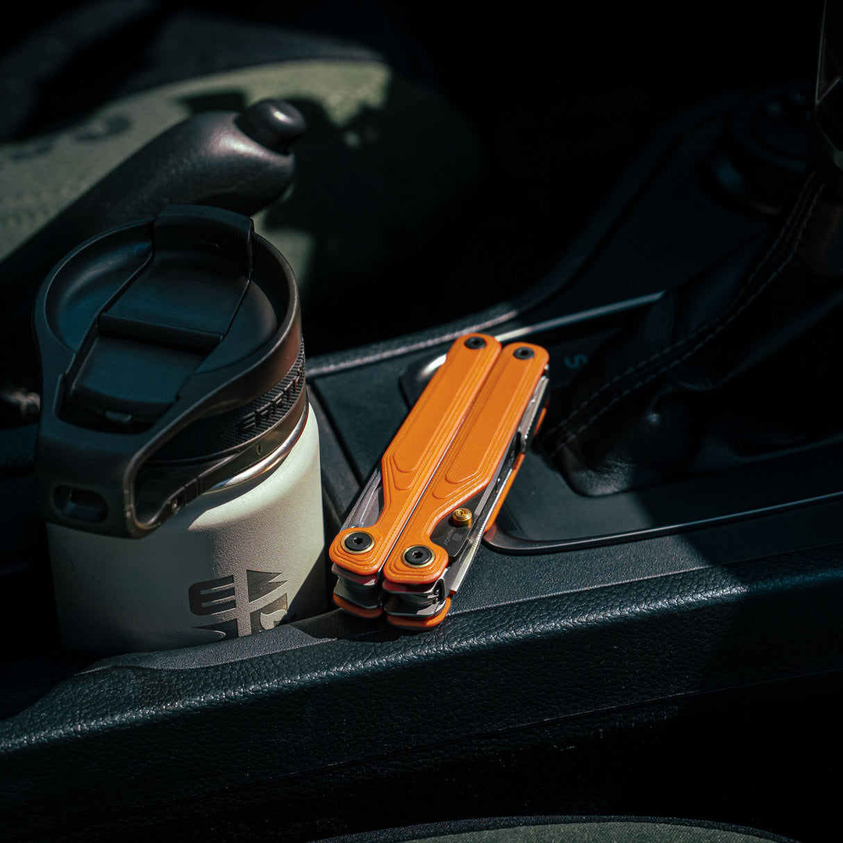 Translation missing: en.Canyonland Leatherman Wave® Alpha multitool beside a stainless steel coffee mug in a car