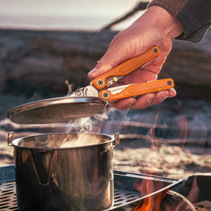 Translation missing: en.Person using Canyonland Leatherman Wave® Alpha multitool to remove a lid from a pot while camping outdoors