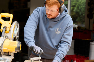 Translation missing: en.A person wearing a storm blue Leatherman Classic Hoodie operating a saw while working on a woodworking project