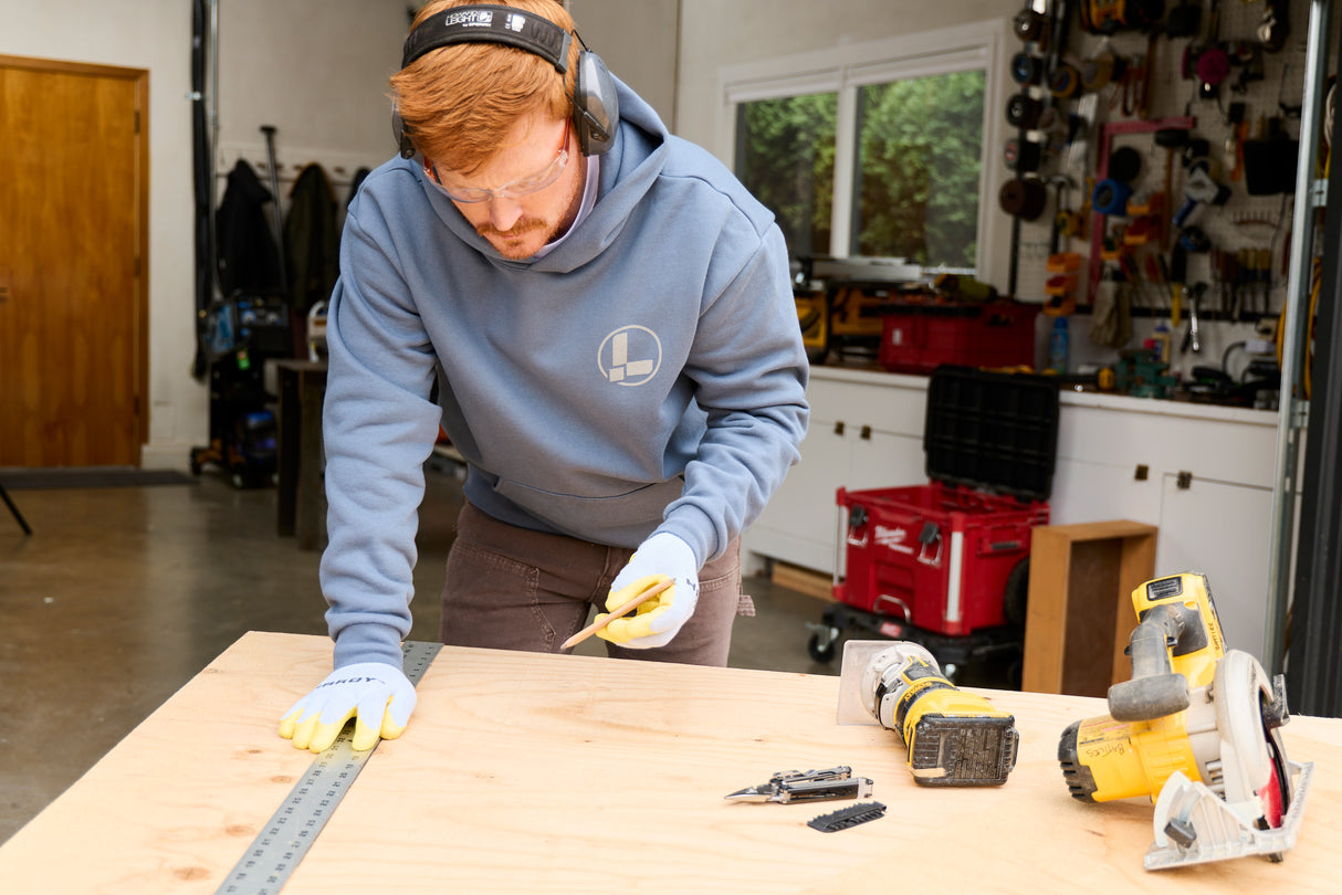 Translation missing: en.A person wearing a Storm Blue Leatherman Classic Hoodie measuring a wooden board in a workshop