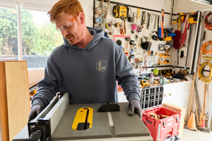 Translation missing: en.A person wearing a storm blue Leatherman Classic Hoodie standing in front of a woodworking tool in a garage workshop
