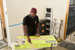 Translation missing: en.A person wearing a black Leatherman Classic Tee using the blade on a Leatherman multi-tool to open a large box that is laying on top of a folding table