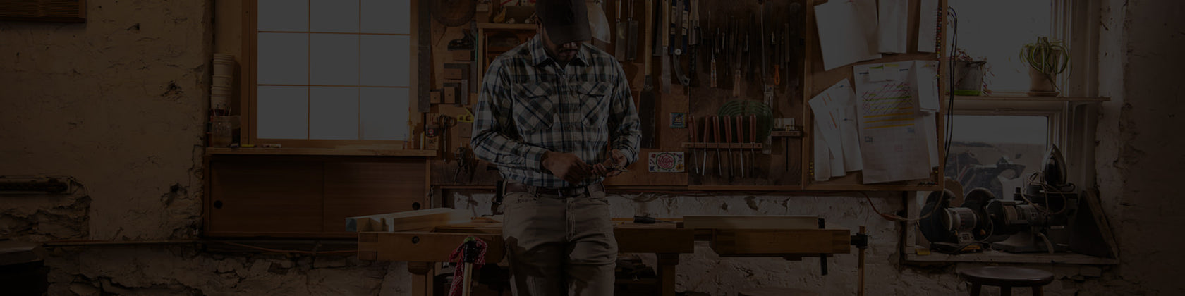Translation missing: en.Craftsperson standing in a rustic woodworking studio using a handheld tool at a workbench surrounded by woodworking equipment, hand tools, and natural light from workshop windows