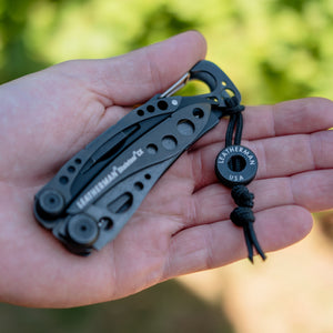 Translation missing: en.Hand holding an Onyx Leatherman Skeletool CX with a lanyard and bead engraved LEATHERMAN USA