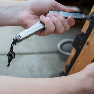 Translation missing: en.Lanyard and bead attached to the deployable leatherman Wave lanyard ring as the tools bit driver is being used on a door