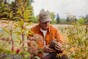 Translation missing: en.A man in a driftwood colored Leatherman Dad Hat inspecting a newly purchased plant before planting