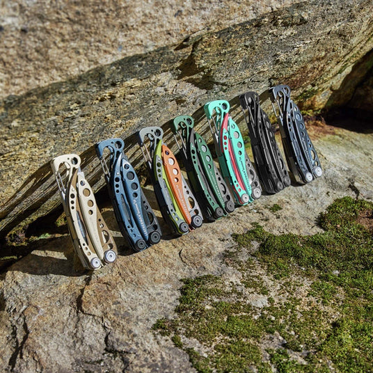 Translation missing: en.Collection of colorful Leatherman Skeletool multi-tools lined up on a rock outdoors