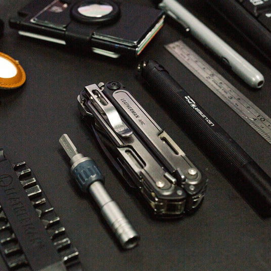 Translation missing: en.Open Leatherman ARC multi-tool displayed on a dark desktop beside tools and accessories