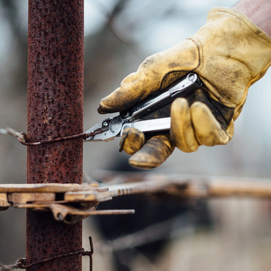 Translation missing: en.Gloved hand using a Leatherman Rebar multi-tool to tighten wire fencing around a metal post