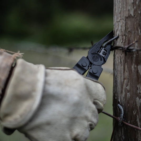 Translation missing: en.Close-up of a Leatherman Super Tool 300 gripping barbed wire on a wooden fence post
