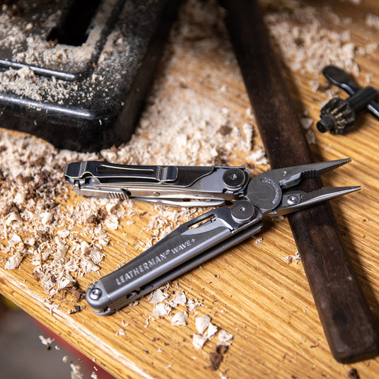 Translation missing: en.Open Leatherman Wave+ multi-tool with pliers extended on a woodworking bench surrounded by sawdust and tools