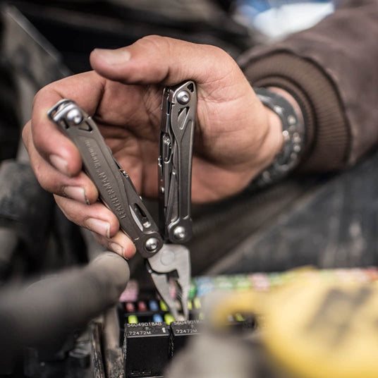 Translation missing: en.Person using a Leatherman Wingman multi-tool for mechanical repair work in a workshop setting