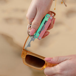 Translation missing: en.Person using the extra small screwdriver on a Leatherman Micra® in Bayside color to tighten sunglasses on the beach