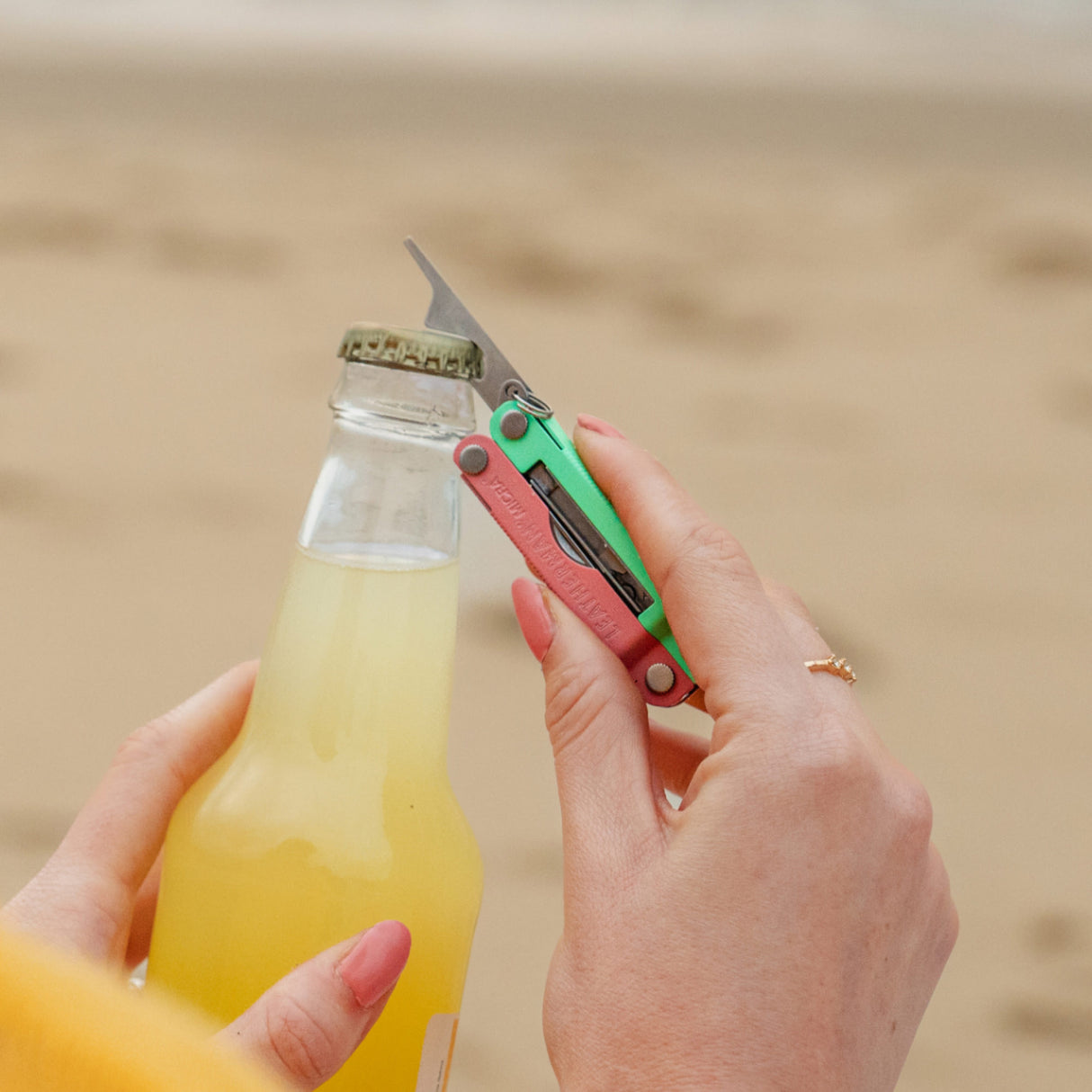 Translation missing: en.Person using the bottle opener on a Leatherman Micra® in Bayside color to open a bottle on the beach