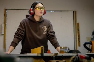 Translation missing: en.A person wearing a brown Leatherman Mr. Wave hoodie standing at a workbench in a workshop, wearing safety glasses and earmuffs