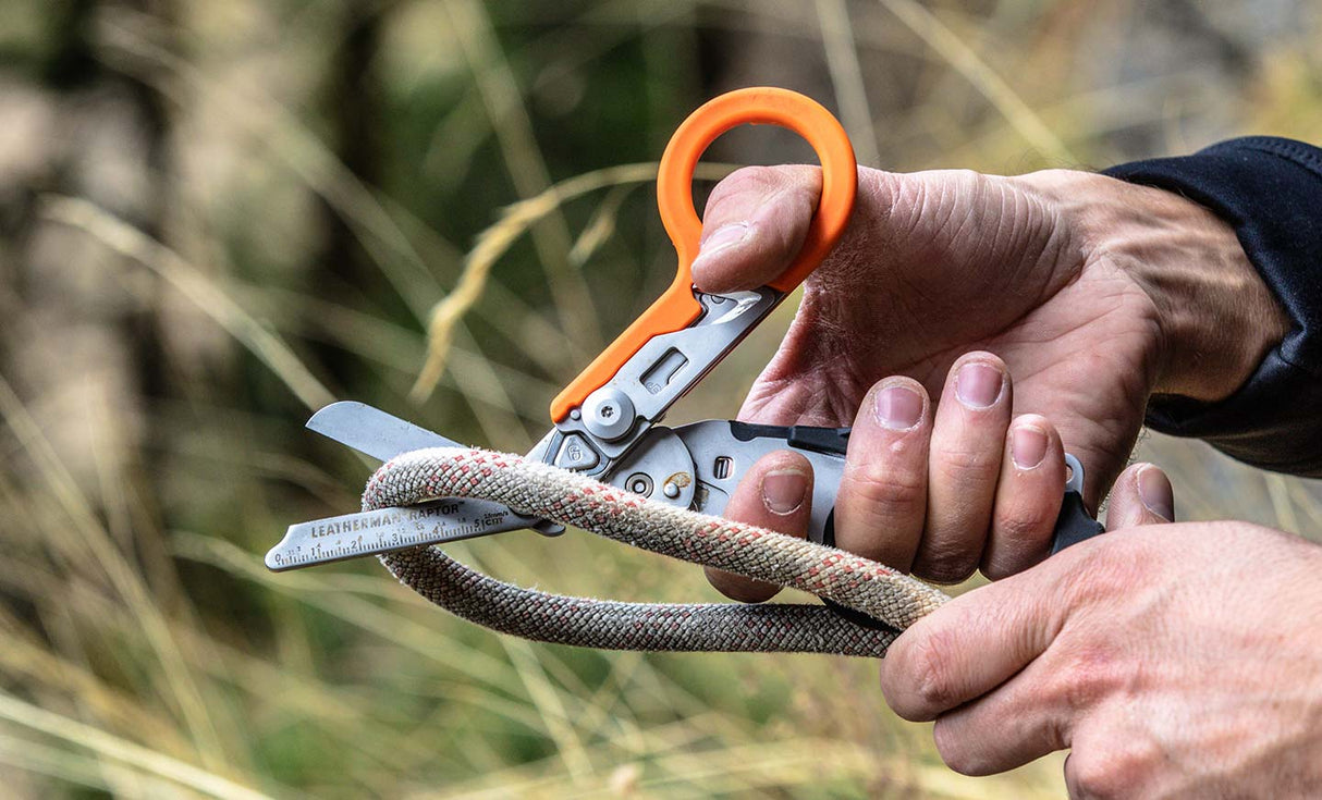 Translation missing: en.Person using an orange and black Leatherman Raptor® Rescue shears to cut a thick rope outdoors