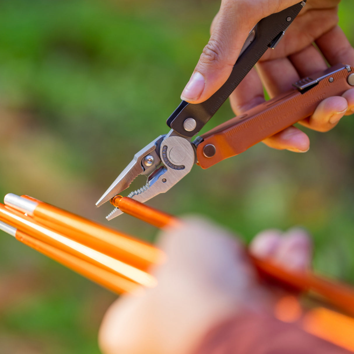 Translation missing: en.Hands using a Burnt Sienna Leatherman Rebar® multi-tool pliers to grip a tent stake, showcasing its functionality in outdoor settings