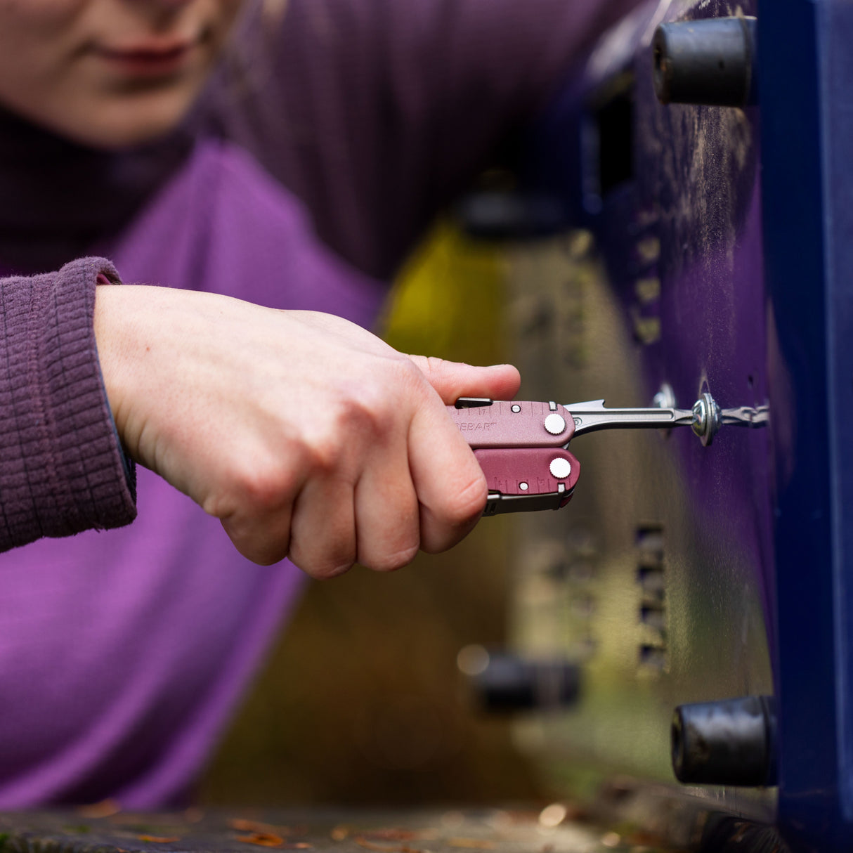 Translation missing: en.Person using a Heathered Cranberry Leatherman Rebar® multitool to tighten a screw outdoors