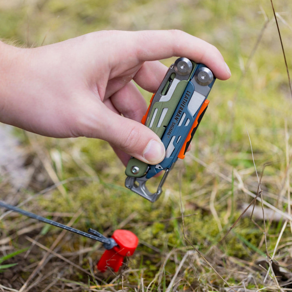 Translation missing: en.A person using the hammer on a Tundrascape Leatherman Signal® to hammer a tent stake in a patch of grass
