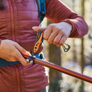 Translation missing: en.Person using a Leatherman Skeletool® CX in Aurora color to adjust a hiking pole outdoors