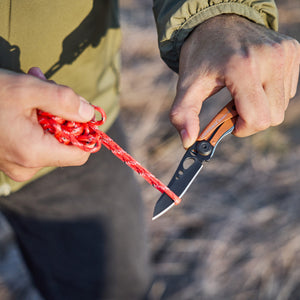 Translation missing: en.Hand using a Aurora Skeletool KB folding knife to cut bright red rope outdoors
