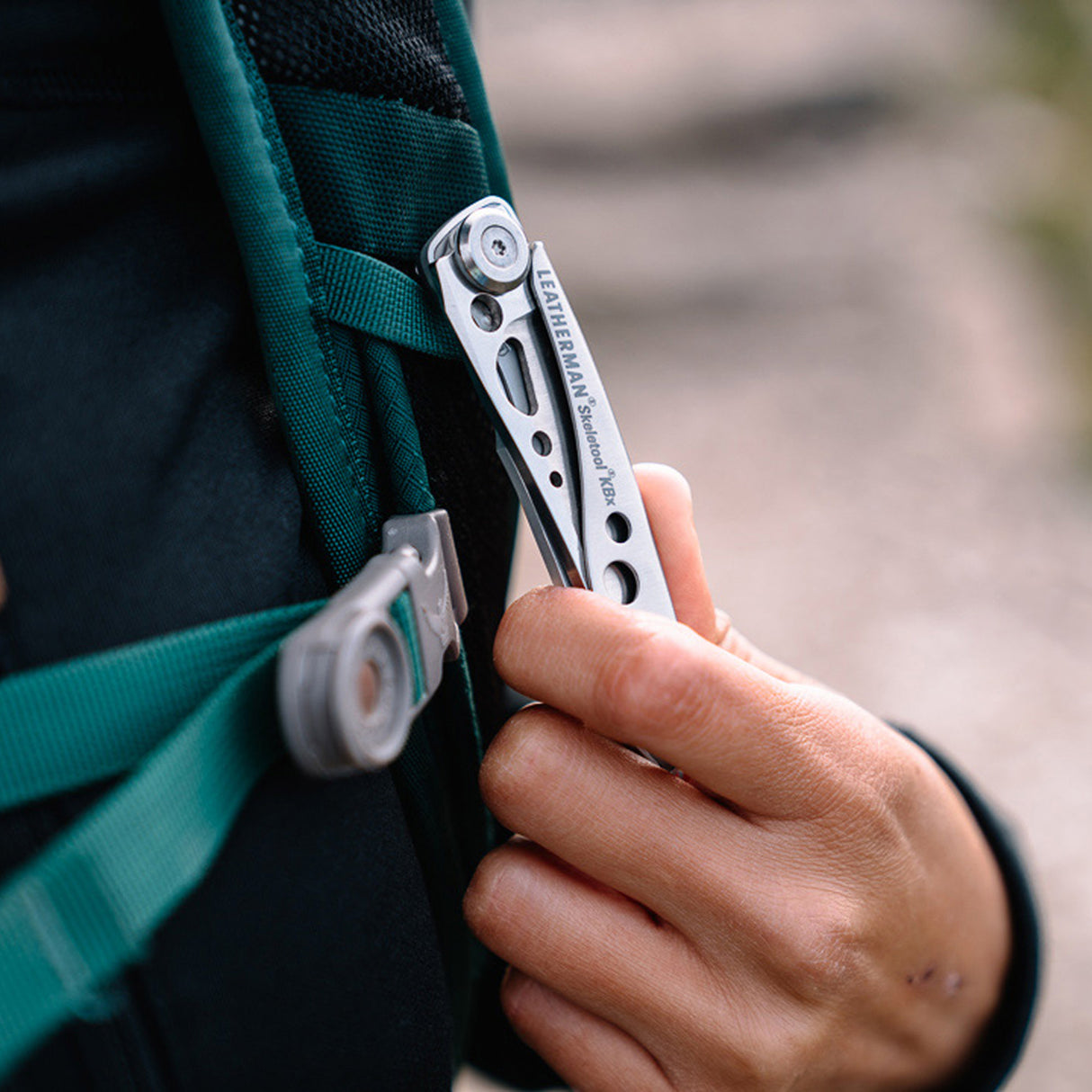 Translation missing: en.Hand clipping a stainless steel Skeletool KBX pocket knife onto a backpack strap