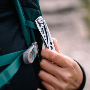 Translation missing: en.Hand clipping a stainless steel Skeletool KBX pocket knife onto a backpack strap