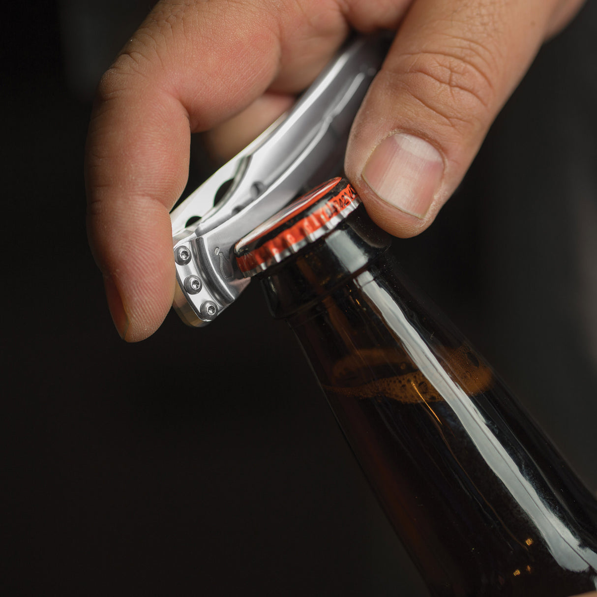 Translation missing: en.Hand using a stainless steel Skeletool KBX to open a capped glass bottle