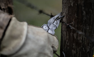 Translation missing: en.Person using a stainless steel Leatherman Surge® multitool pliers on barbed wire attached to a wooden post