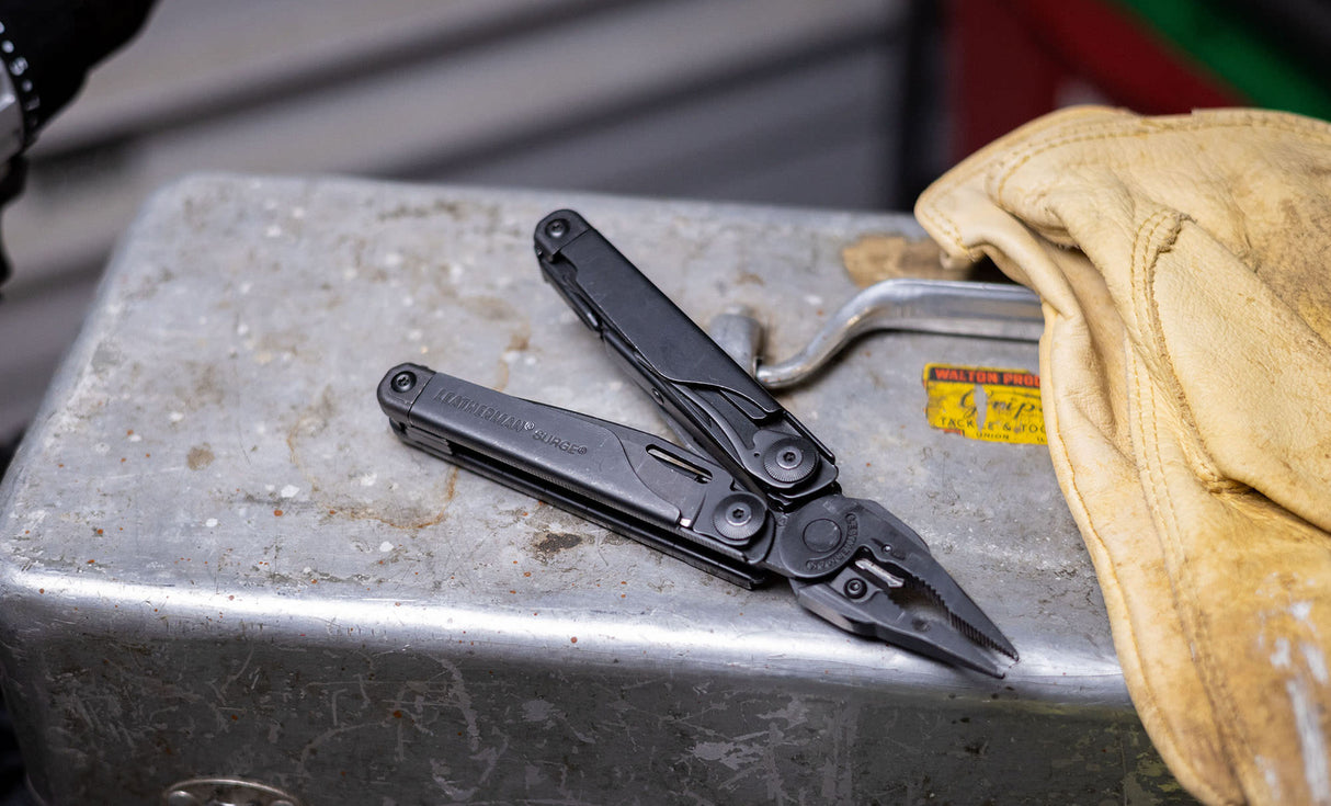 Translation missing: en.Black Leatherman Surge® multi-tool resting on a metal toolbox beside gloves