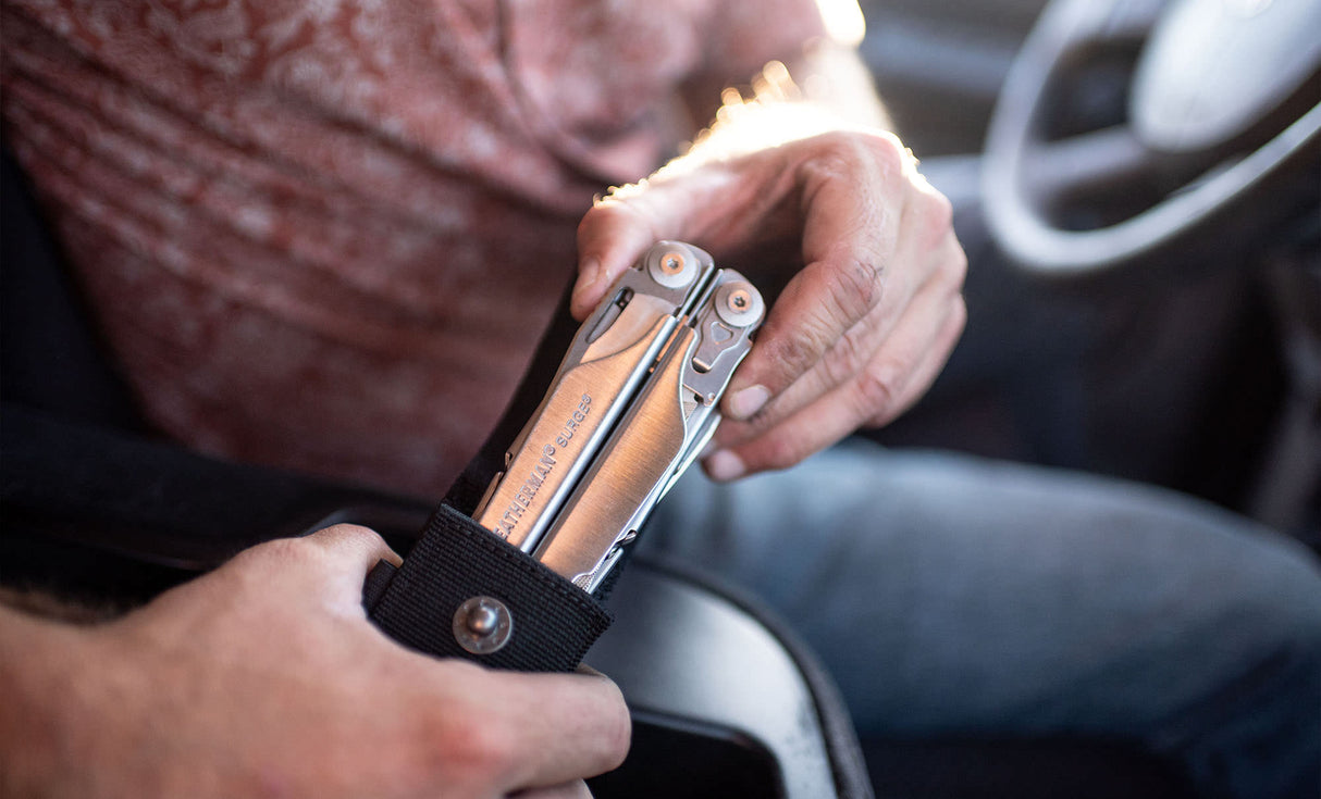 Translation missing: en.Person pulling a stainless steel Leatherman Surge® multitool from its sheath while sitting in a car