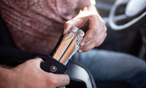 Translation missing: en.Person pulling a stainless steel Leatherman Surge® multitool from its sheath while sitting in a car