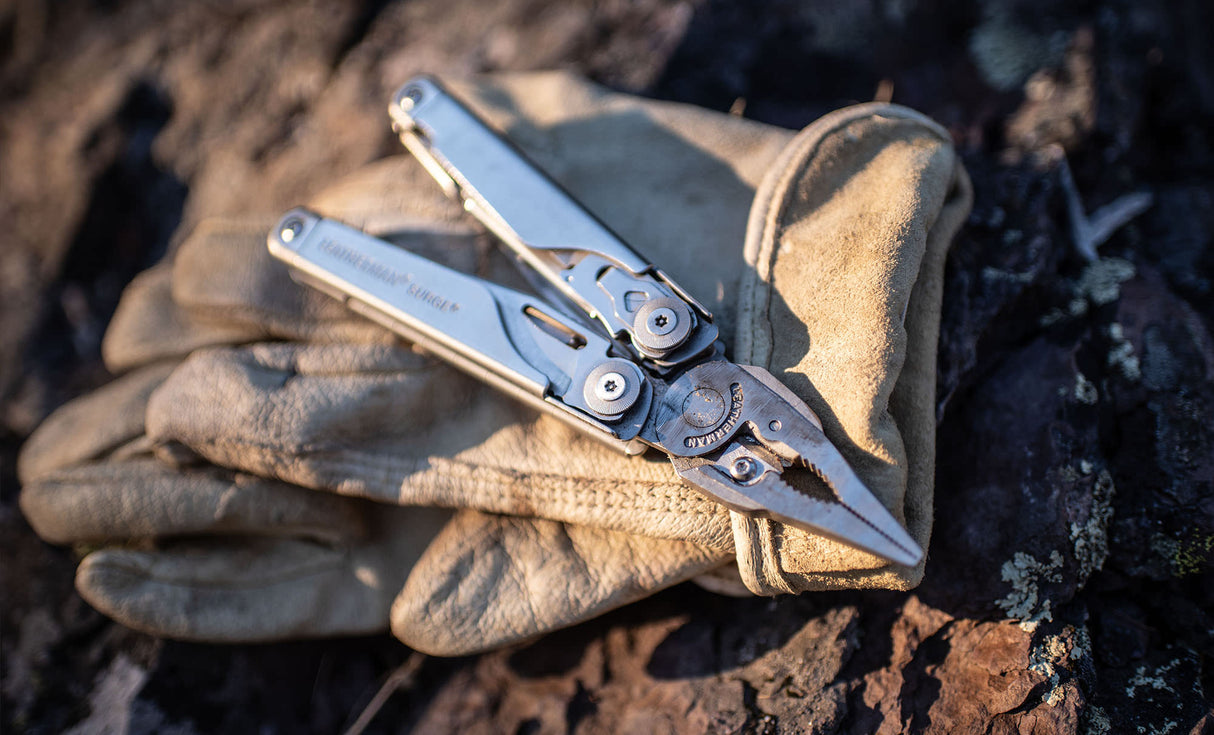 Translation missing: en.Stainless steel Leatherman Surge® multi-tool resting on a leather glove atop a rugged surface