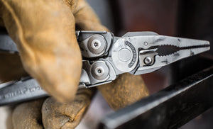 Translation missing: en.Close up of a hand holding stainless steel Leatherman Surge® multitool with pliers and gloves