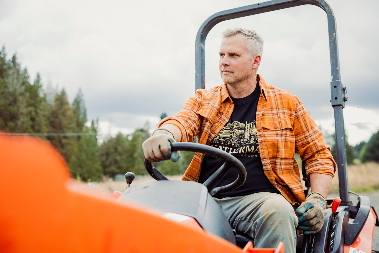 Translation missing: en.A person wearing a black Leatherman Timber Tee driving a tractor outdoors