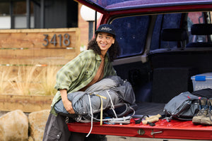 Translation missing: en.A woman wearing a black Leatherman Vintage 5-Panel Hat loading camping gear into the back of a red vehicle, smiling while preparing for an outdoor trip