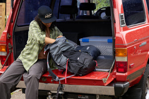 Translation missing: en.A woman wearing a black Leatherman Vintage 5 Panel Hat packing a backpack on the open tailgate of a red vehicle