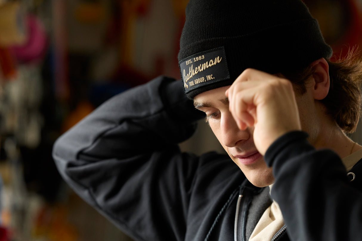 Translation missing: en.A person adjusting a black Leatherman Vintage Beanie while indoors, with the gold embroidered Leatherman logo visible on the front patch